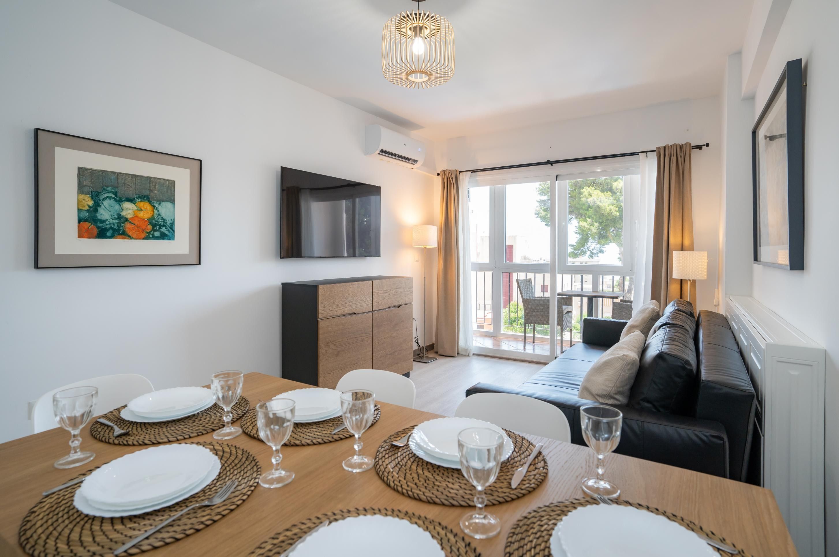 A dining area with a table set for four, a sofa, a TV, and a window with curtains.
