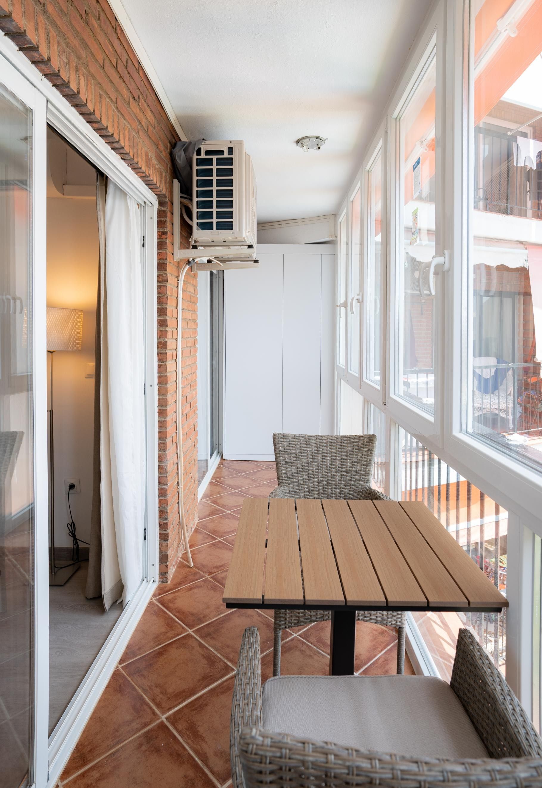 A balcony with a table and chairs, an air conditioning unit, and a view of the outside.