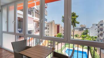 Un balcon avec une table et des chaises, donnant sur une piscine et des immeubles d’habitation.