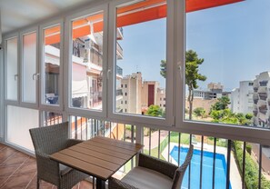 Un balcon avec une table et des chaises, donnant sur une piscine et des immeubles d’habitation.