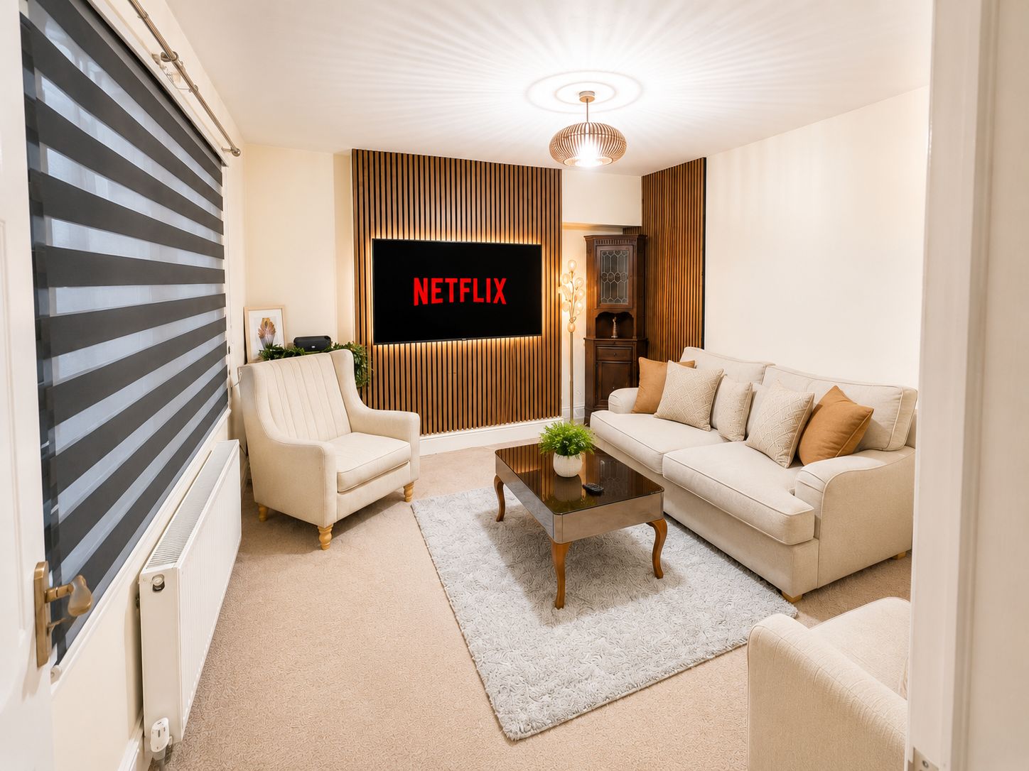 A living room with a sofa, armchair, coffee table, and a television displaying 'NETFLIX'.