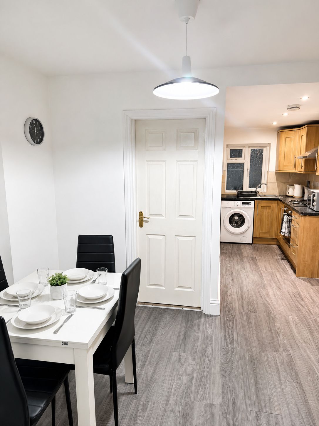 A modern kitchen with a washing machine, wooden cabinets, and a dining area with a white table and black chairs.