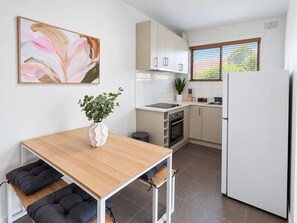 A modern kitchen with white cabinets, a wooden table, and a white refrigerator. - Chic St Kilda retreat with secure parking (St Kilda)