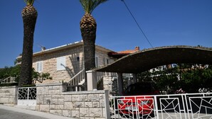 A stone building with a covered entrance, palm trees, and a gated driveway. - A2 Apartment with terrace, 1 min walking to the beach (Supetar)