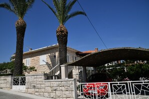Un bâtiment en pierre doté d’une entrée couverte, de palmiers et d’une allée bordée de portails.