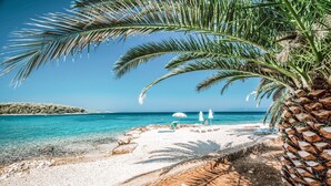 A beach with clear turquoise water, white sand, and a palm tree. - A2 Apartment with terrace, 1 min walking to the beach (Supetar)