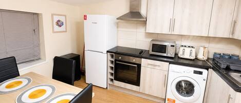 A compact kitchen with a refrigerator, microwave, toaster, and washing machine.