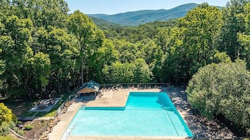 Una piscina rectangular con área de terraza, rodeada de exuberante follaje y árboles.