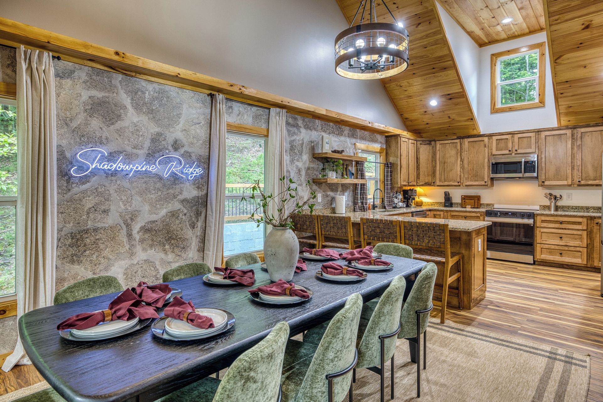 A dining area with a long table set for a meal, wooden cabinets, and a stone wall with a neon sign.