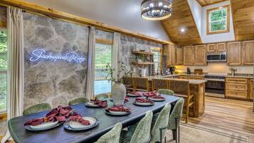 A dining area with a long table set for a meal, wooden cabinets, and a stone wall with a neon sign.