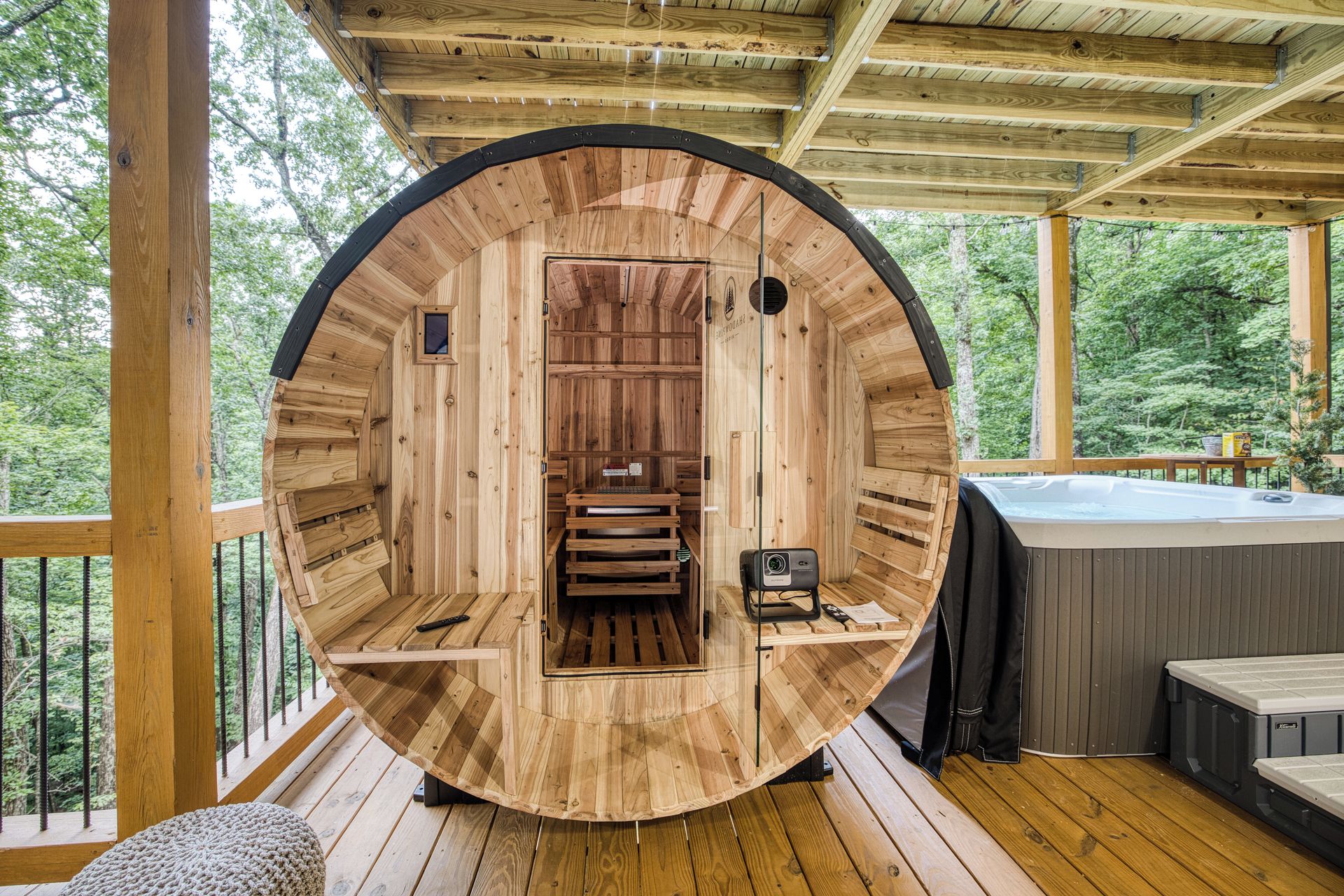 A wooden sauna with a bench, a control panel, and a hot tub outside.