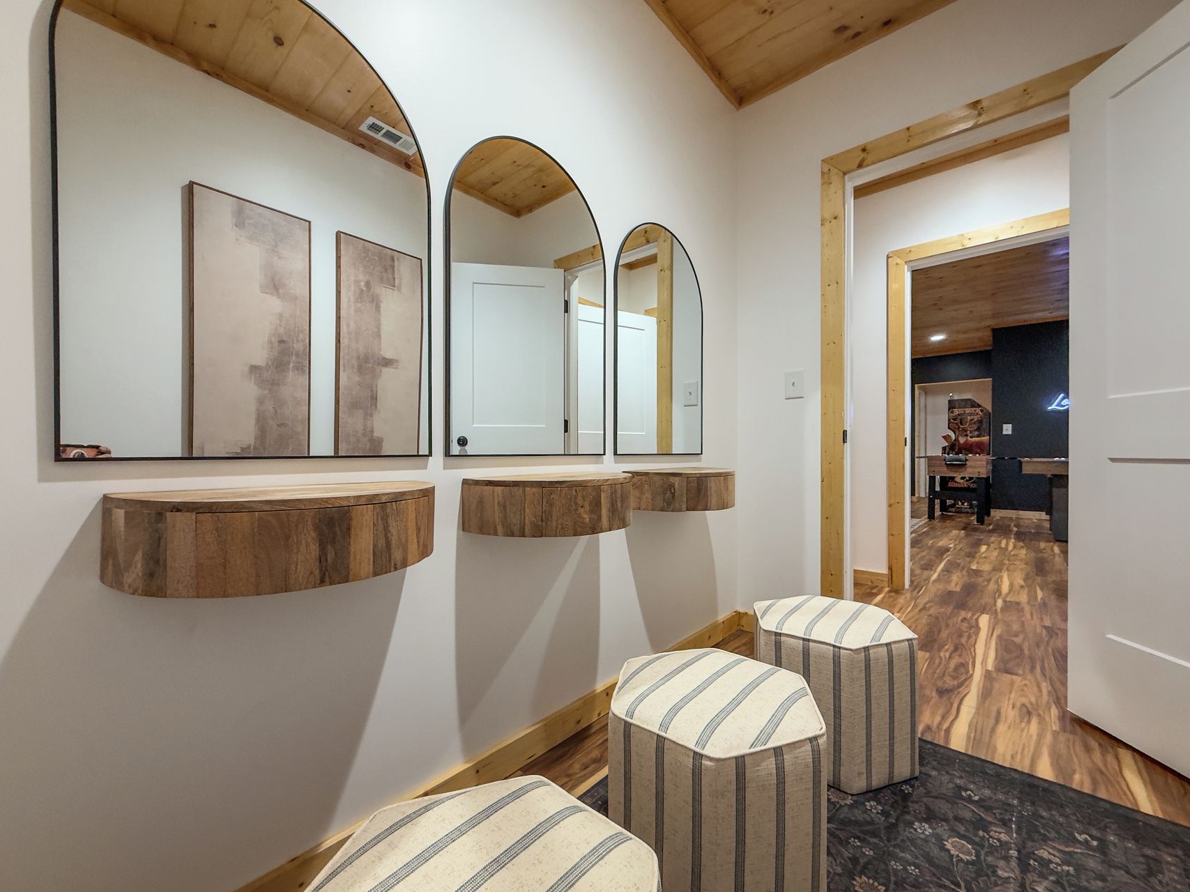 A hallway with wooden beams, a mirror with artwork, and a door leading to a room with a pool table.