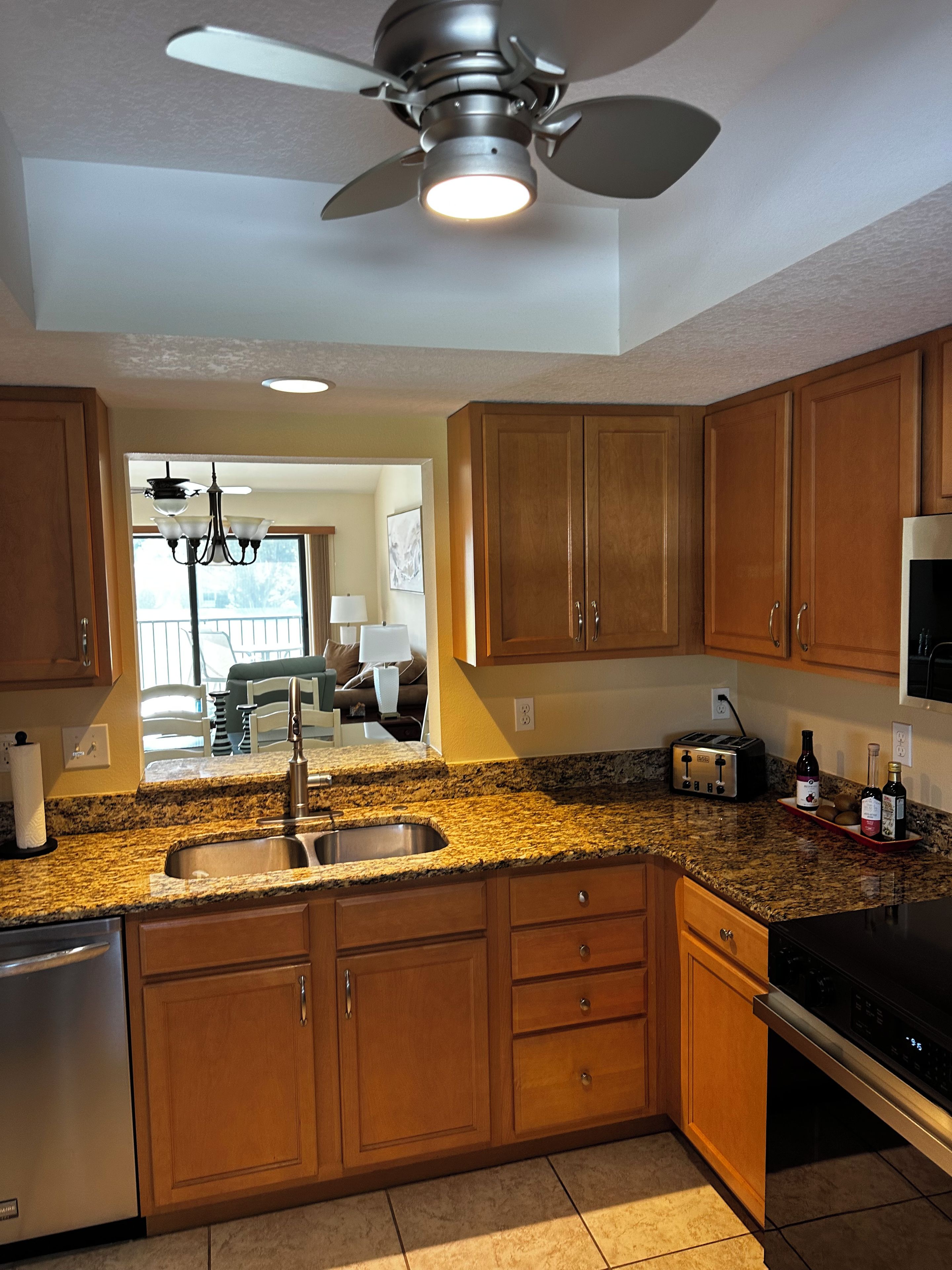 A kitchen with wooden cabinets, granite countertops, a built-in dishwasher, and a ceiling fan.