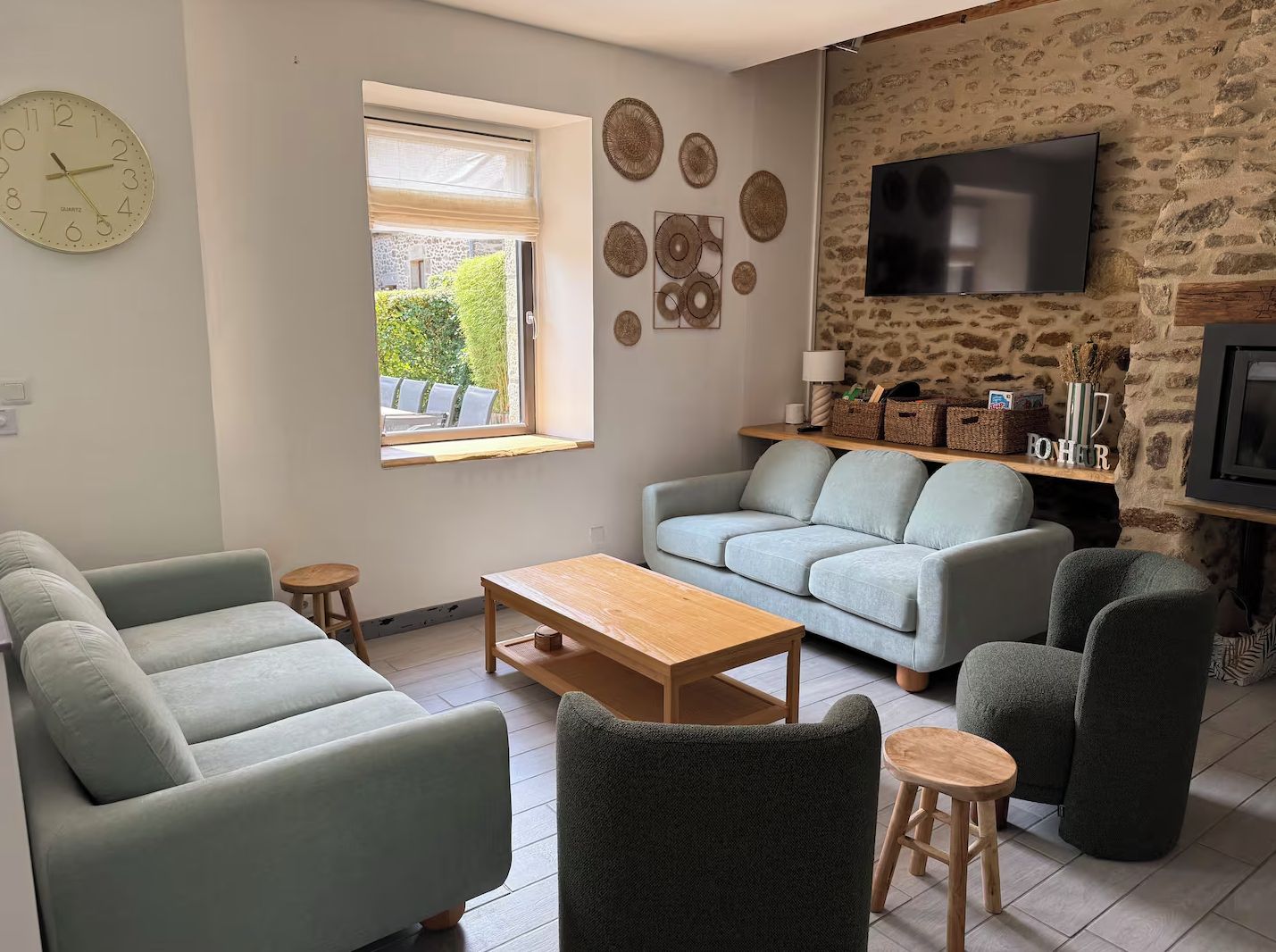 A living room with a sofa, armchairs, a coffee table, a TV, and a stone wall.