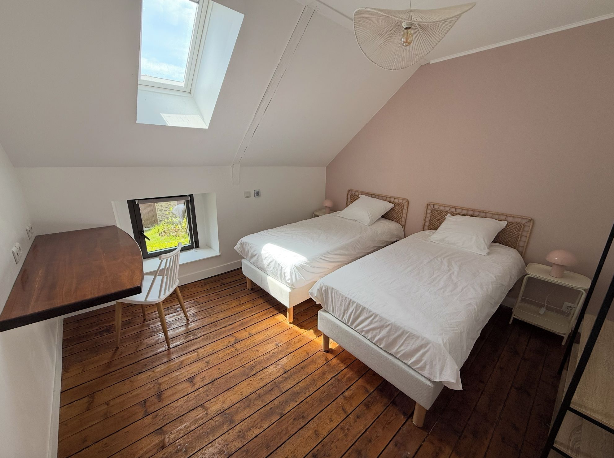 A bedroom with two single beds, a wooden desk, a chair, a window with a view, and a ceiling fan.