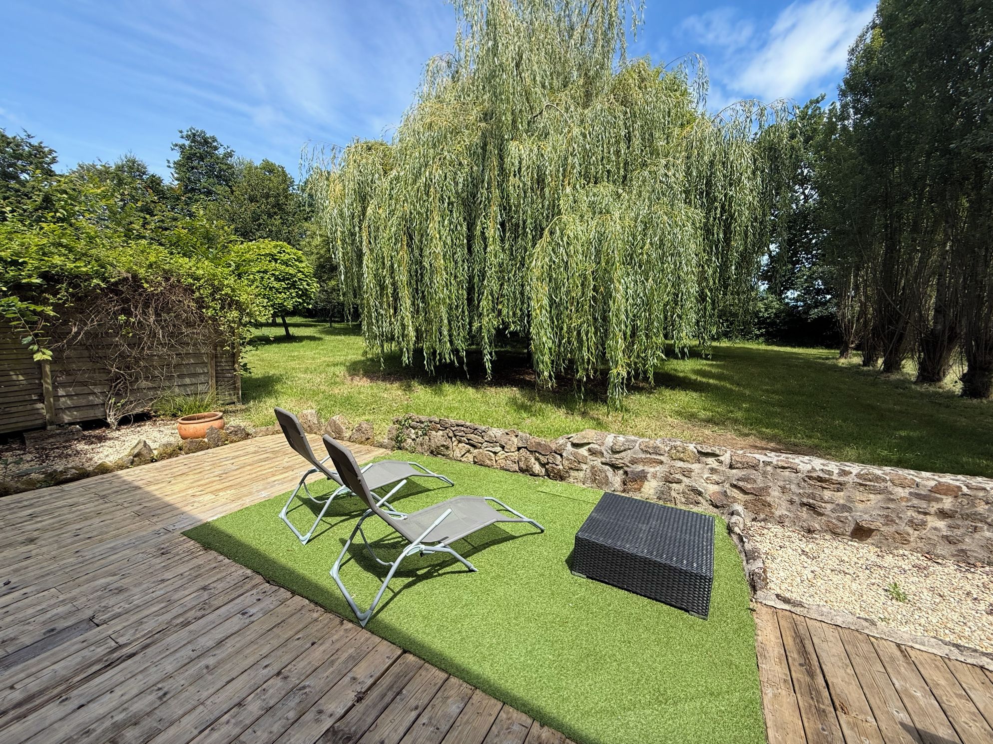 Una terraza de madera con césped artificial, dos sillas de metal y una pequeña mesa.