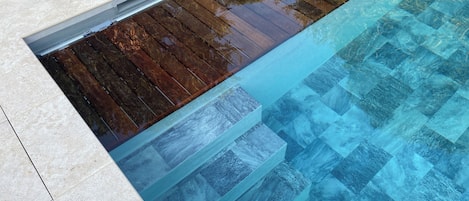 Una piscina con agua cristalina, cubierta de madera y suelo de baldosas.