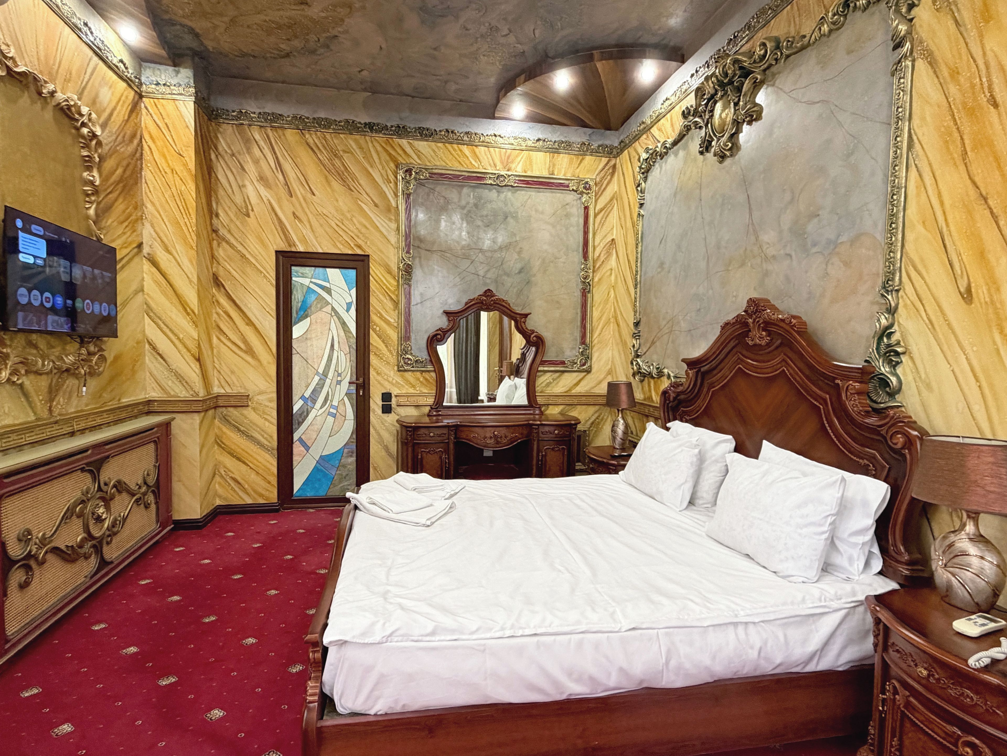 Ein Hotelzimmer mit einem großen Bett, einem hölzernen Schminktisch, einem Spiegel und einem Fernseher an der Wand.