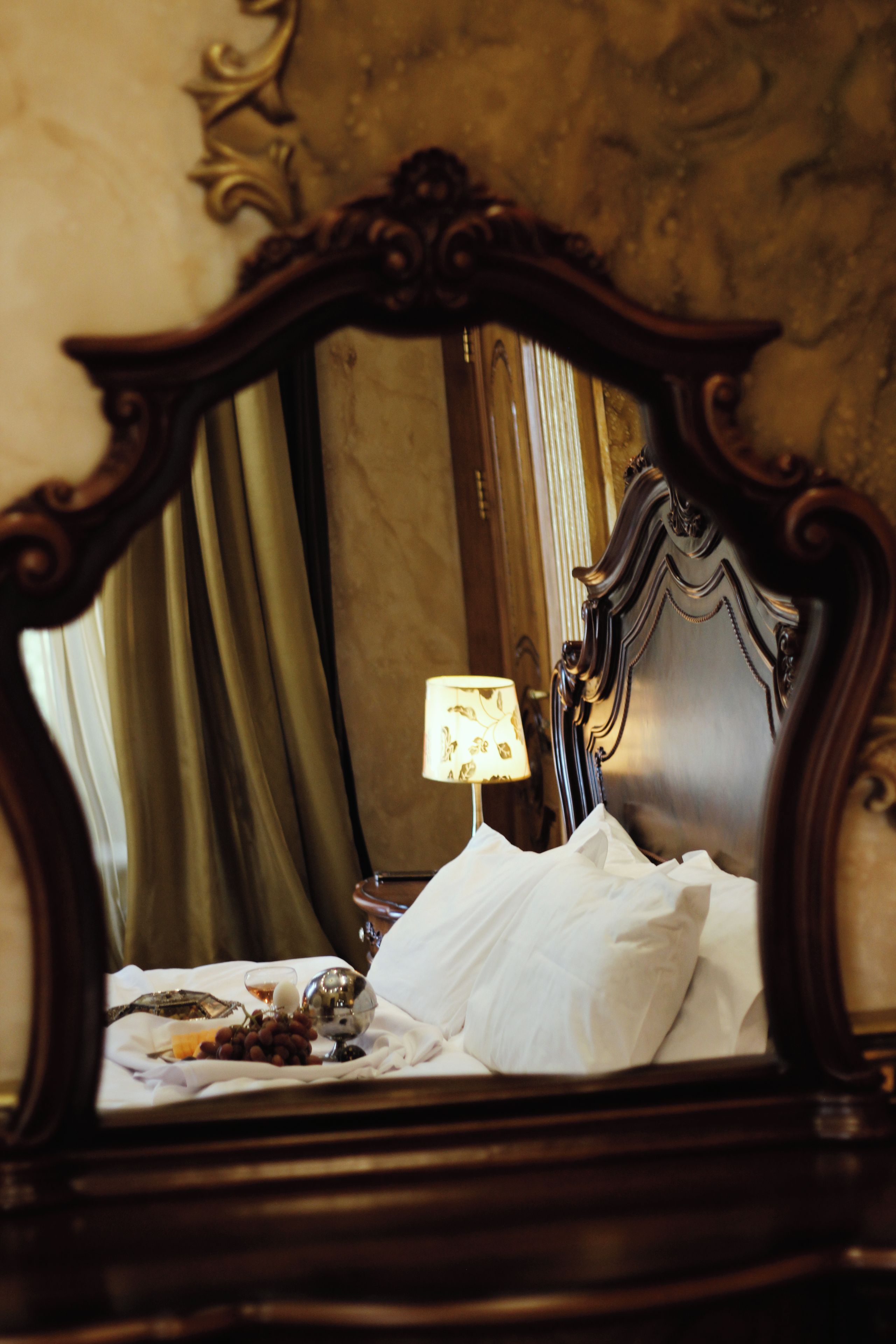 A bed with a white pillow and a decorative mirror above it.
