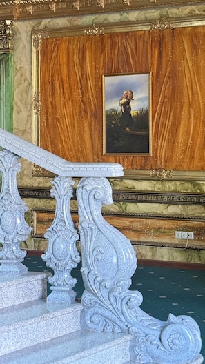 A staircase with ornate white balustrades leading to a room with a wooden panel wall and a framed painting. - Alexandrapol Hotel Palace (Gyumri)