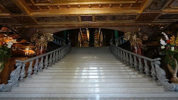 Eine prachtvolle Treppe mit aufwendiger Balustrade und einem Chandelier, die zu einem abgedunkelten Raum mit hoher Decke führt.