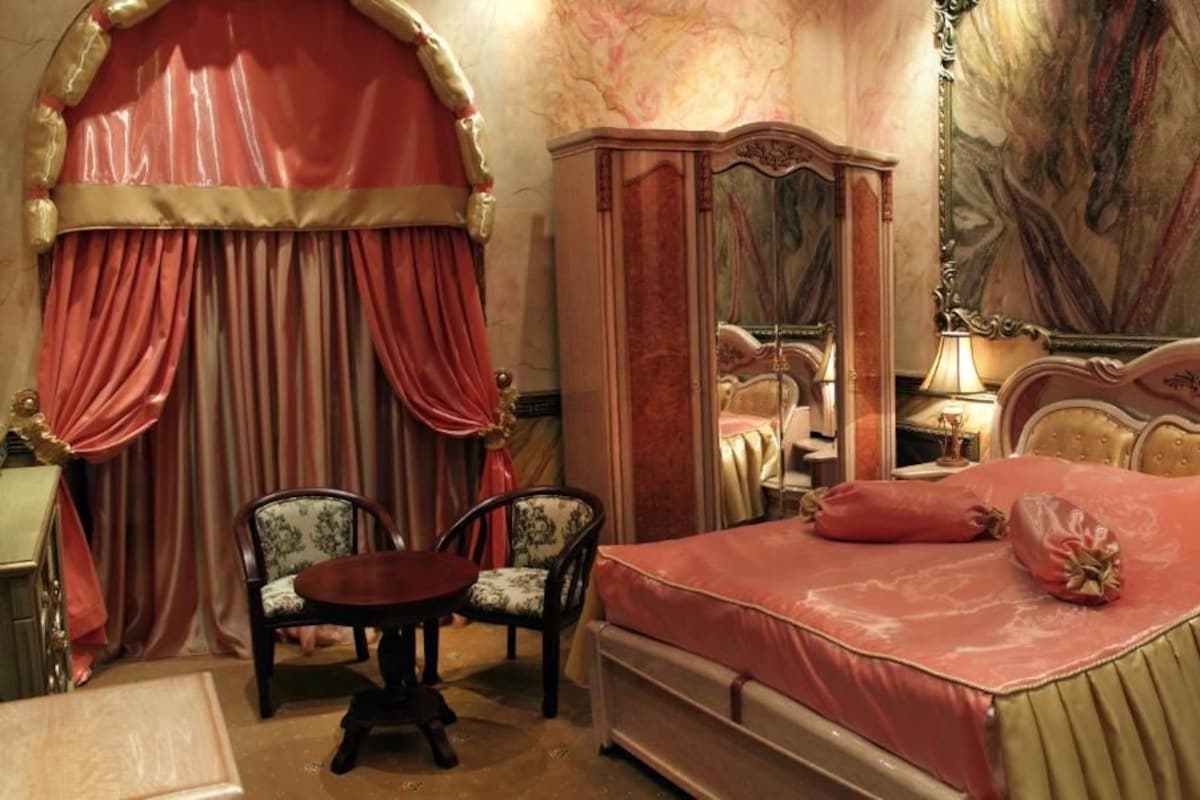 Een slaapkamer met een bed, een stoel, een tafel, een kledingkast en een groot schilderij aan de muur.