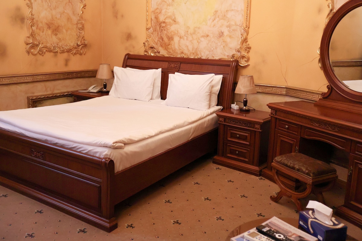 A hotel room with a large bed, two bedside tables, a wooden dresser, and a mirror.