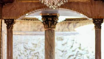 A grand chandelier with multiple lights, a marble column, and a classical architectural backdrop.