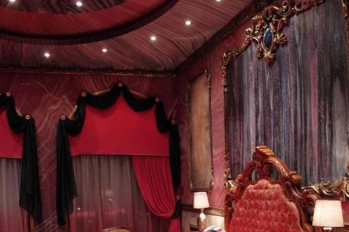 Een kamer met een groot bed, een versierd hoofdeinde en rode gordijnen.