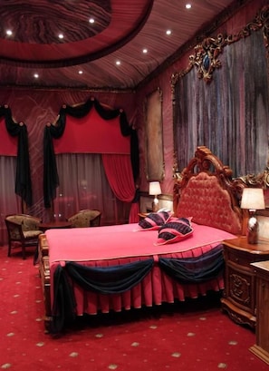 Een kamer met een groot bed, een versierd hoofdeinde en rode gordijnen.