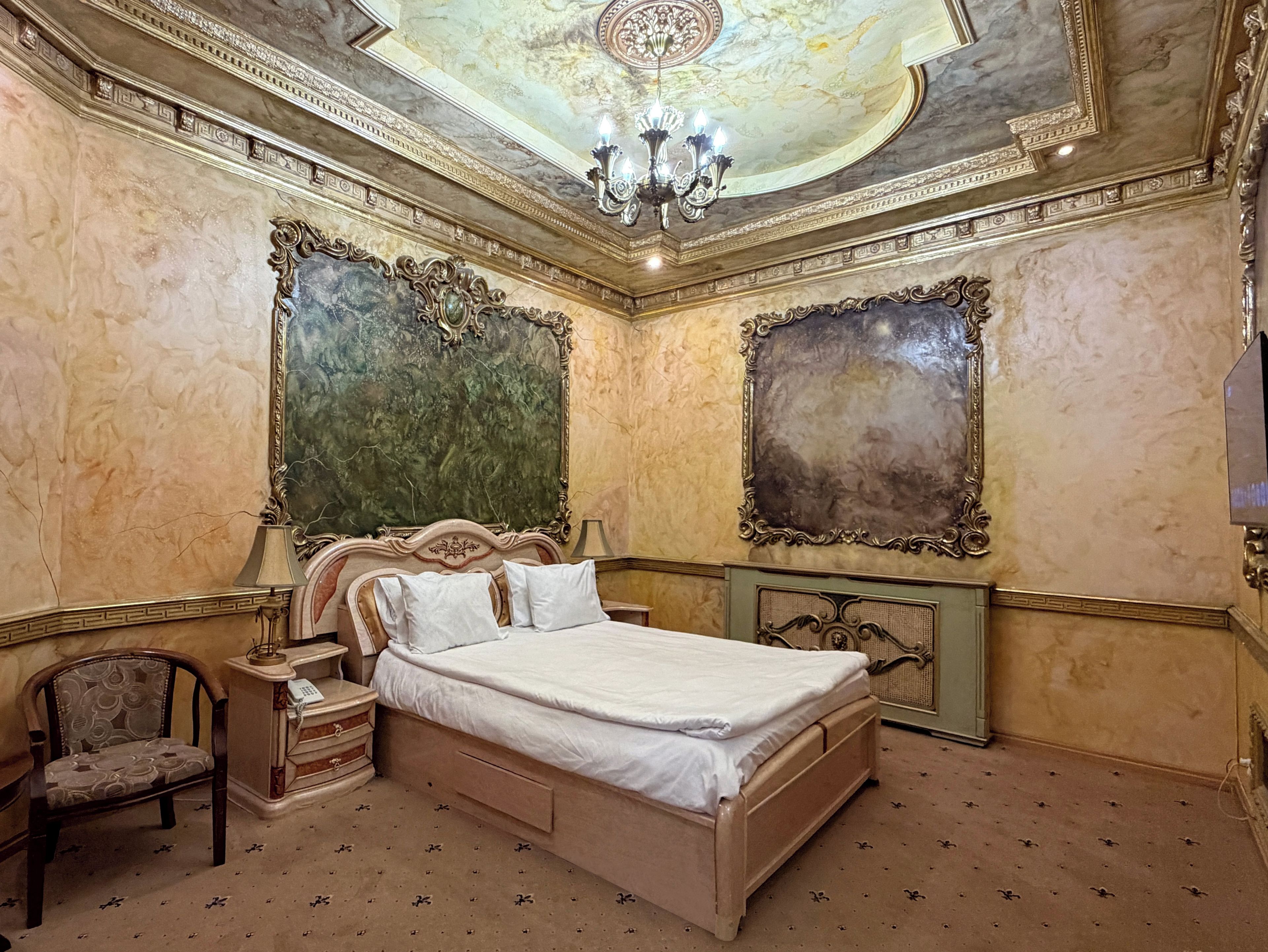 A bedroom with a large bed, ornate wall decorations, and a chandelier.