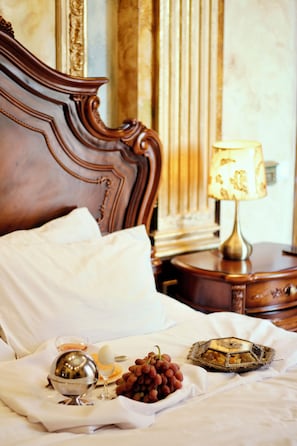 A neatly made bed with pillows, a bedside table with a lamp, and a tray with grapes and a silver bowl. - Alexandrapol Hotel Palace (Gyumri)