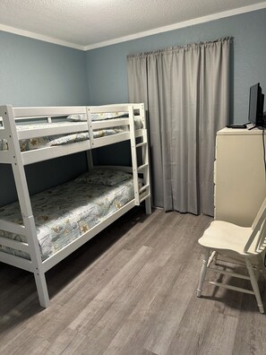 Ein Etagenbett mit Schreibtisch und Stuhl, ein Fenster mit Vorhängen und ein Holzboden.