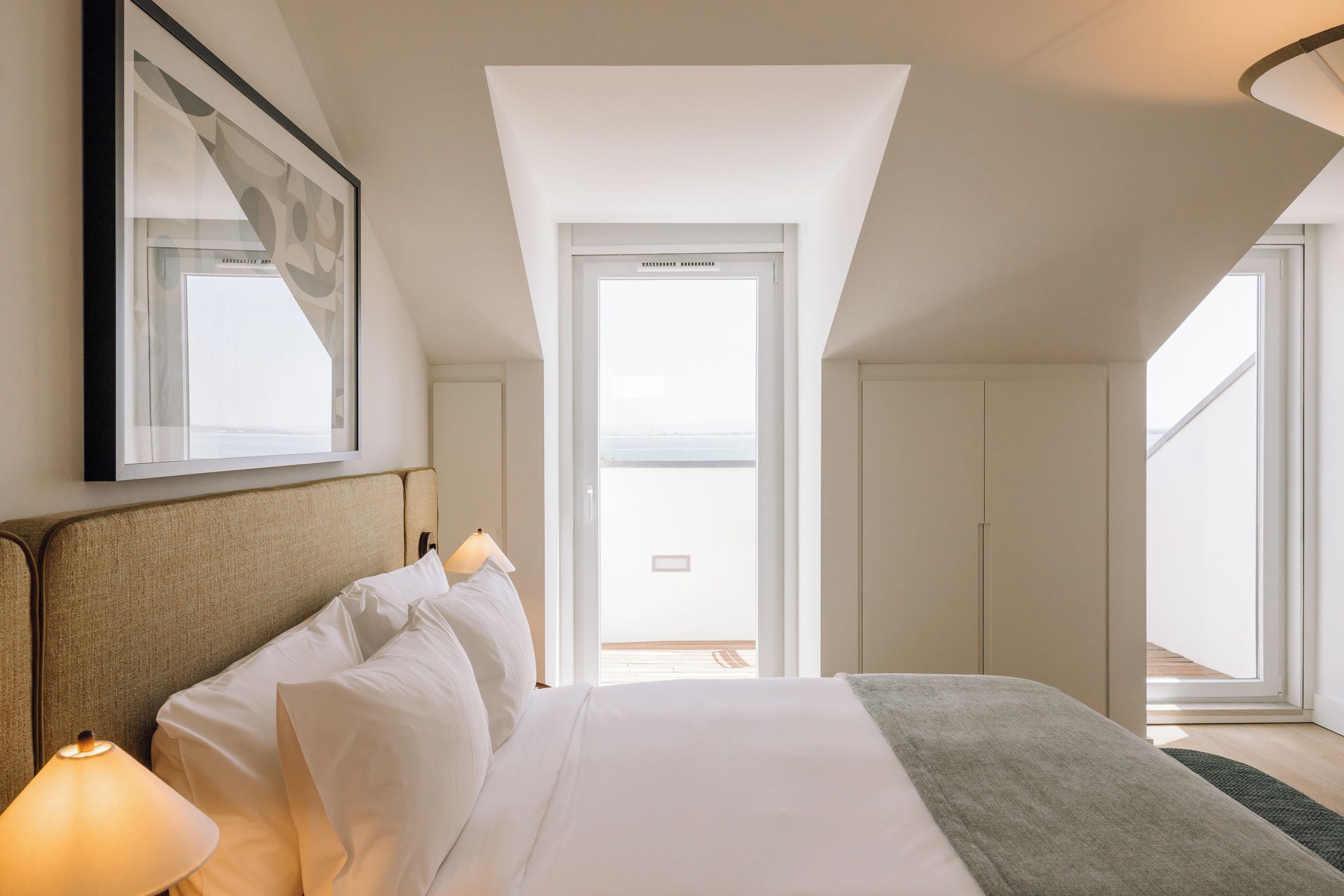 Une chambre d’hôtel avec un lit, des lampes de chevet, un tableau encadré et une vue sur l’extérieur.