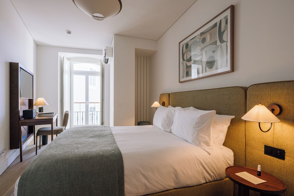 A hotel room with a large bed, bedside lamps, a desk with a chair, a television, and a painting on the wall.