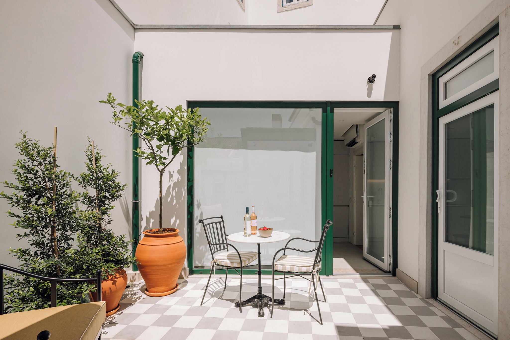 Eine Terrasse mit Schachbrettmuster, einem Tisch mit Stühlen, einer Topfpflanze und einem großen Terrakottatopf.