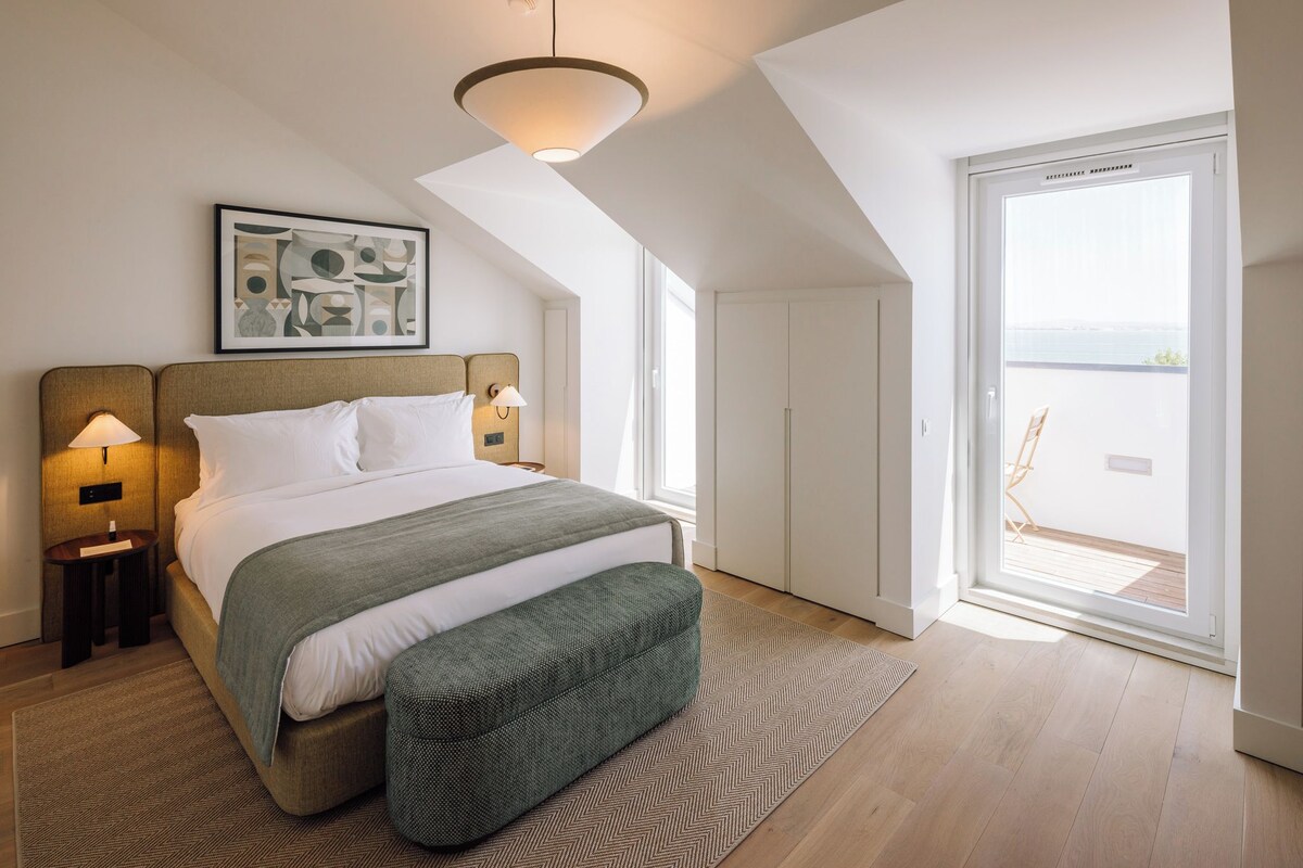 A bedroom with a bed, bedside lamps, a large window, and a view of the outdoors.