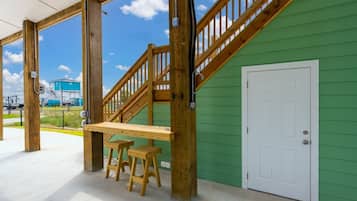 A covered outdoor area with a wooden bench and a staircase leading to a green building.