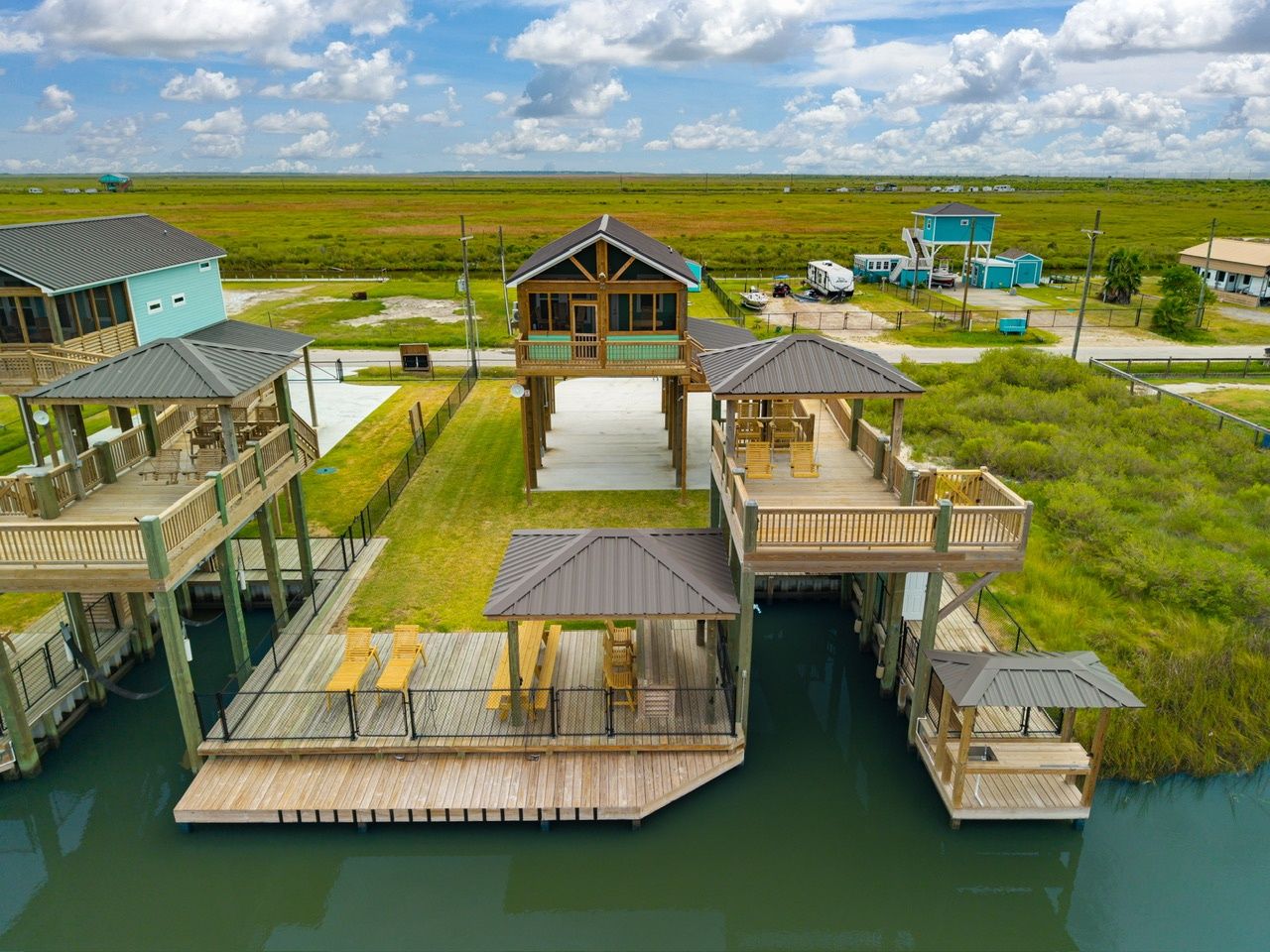 A waterfront property with multiple docked structures, a central building with a covered deck, and a surrounding grassy landscape.