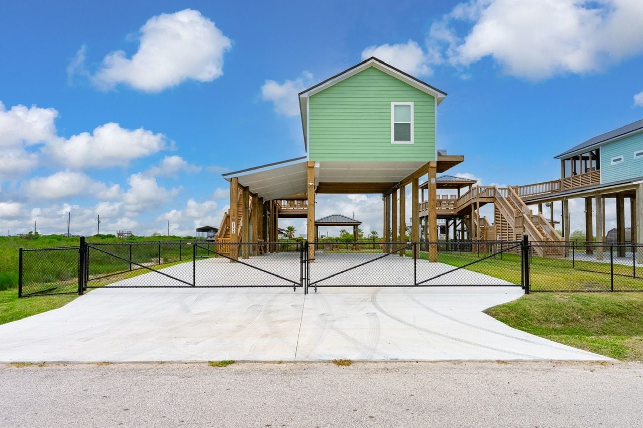 A beachfront property with a covered deck, a staircase leading to a second level, and a gated entrance.