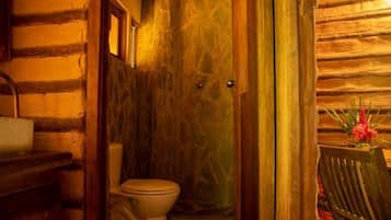 Ein Holzblockhaus-Innenraum mit Toilette, einer Holzbank und einem kleinen Tisch mit Blumenvase.