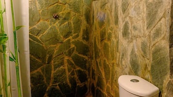 Un baño con pared de piedra, inodoro y cortina de ducha con estampado de bambú.