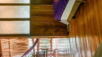 A room with wooden floors, a bed with a patterned blanket, a window with frosted glass, and a view of the outdoors.