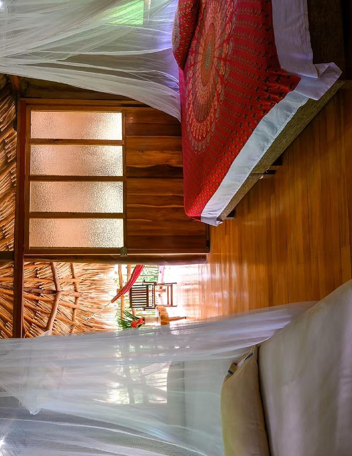 Quarto com cama, janela com vidro jateado e piso de madeira.