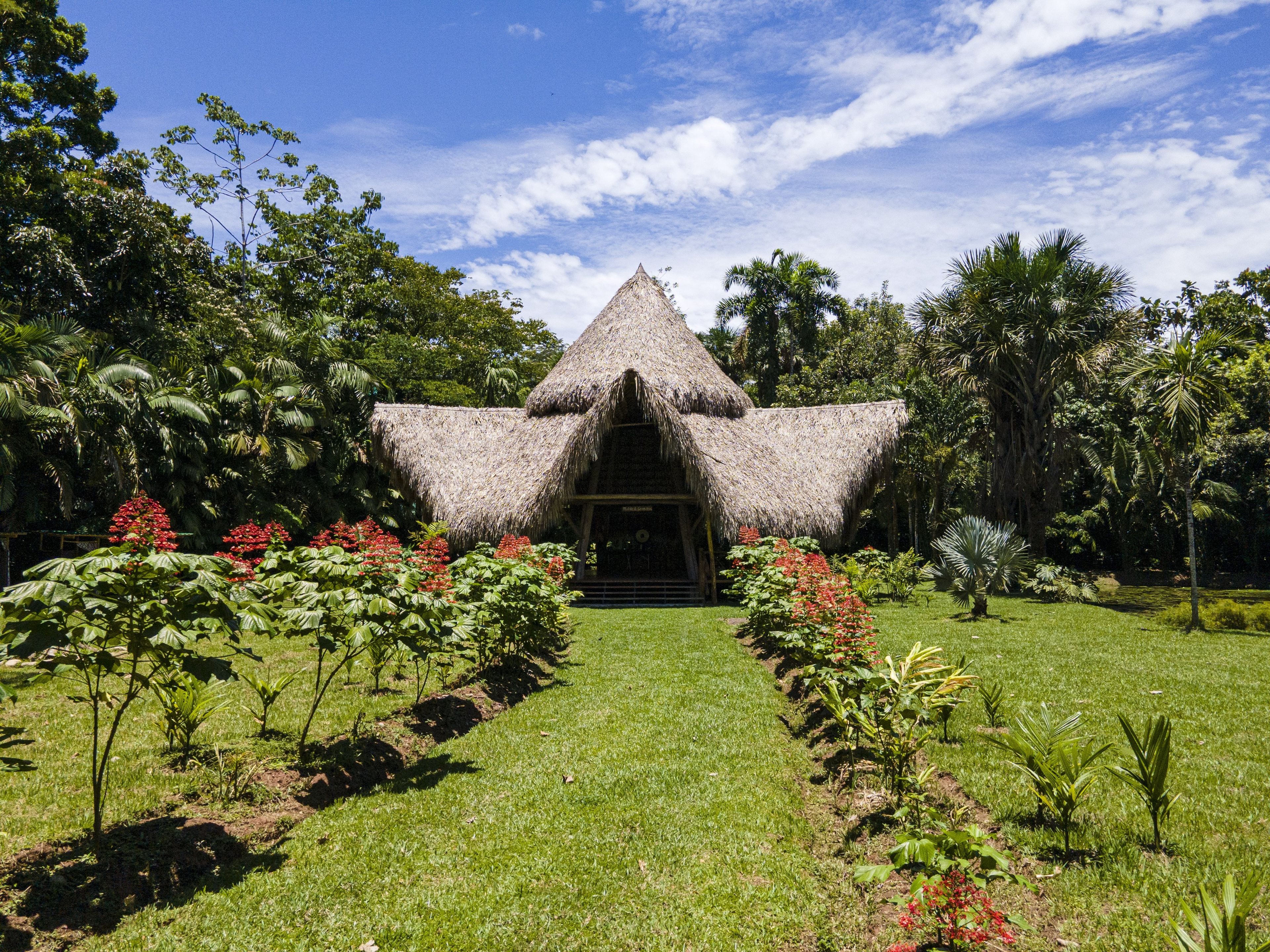 A thatched-roof structure with a central entrance, surrounded by a well-maintained garden with various plants and flowers.