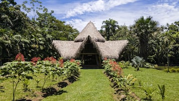 A thatched-roof structure with a central entrance, surrounded by a well-maintained garden with various plants and flowers.
