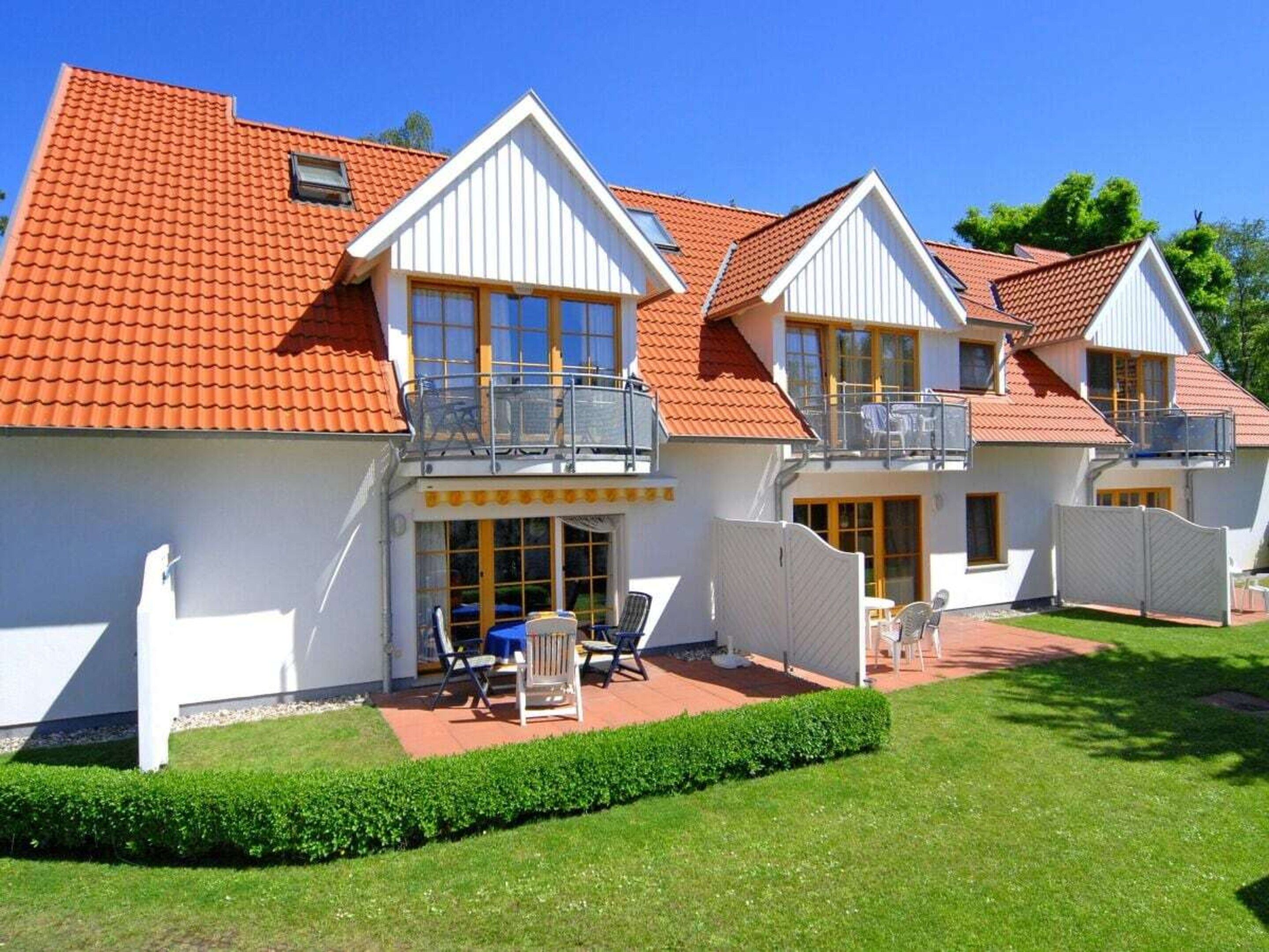 A two-story house with a red-tiled roof, white exterior walls, and a fenced patio area with outdoor furniture.
