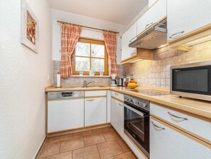 A compact kitchen with white cabinets, a built-in oven, a microwave, and a window with curtains. - 3.4/t3 Holiday Home Park \"freesenbruch\" (Zingst)