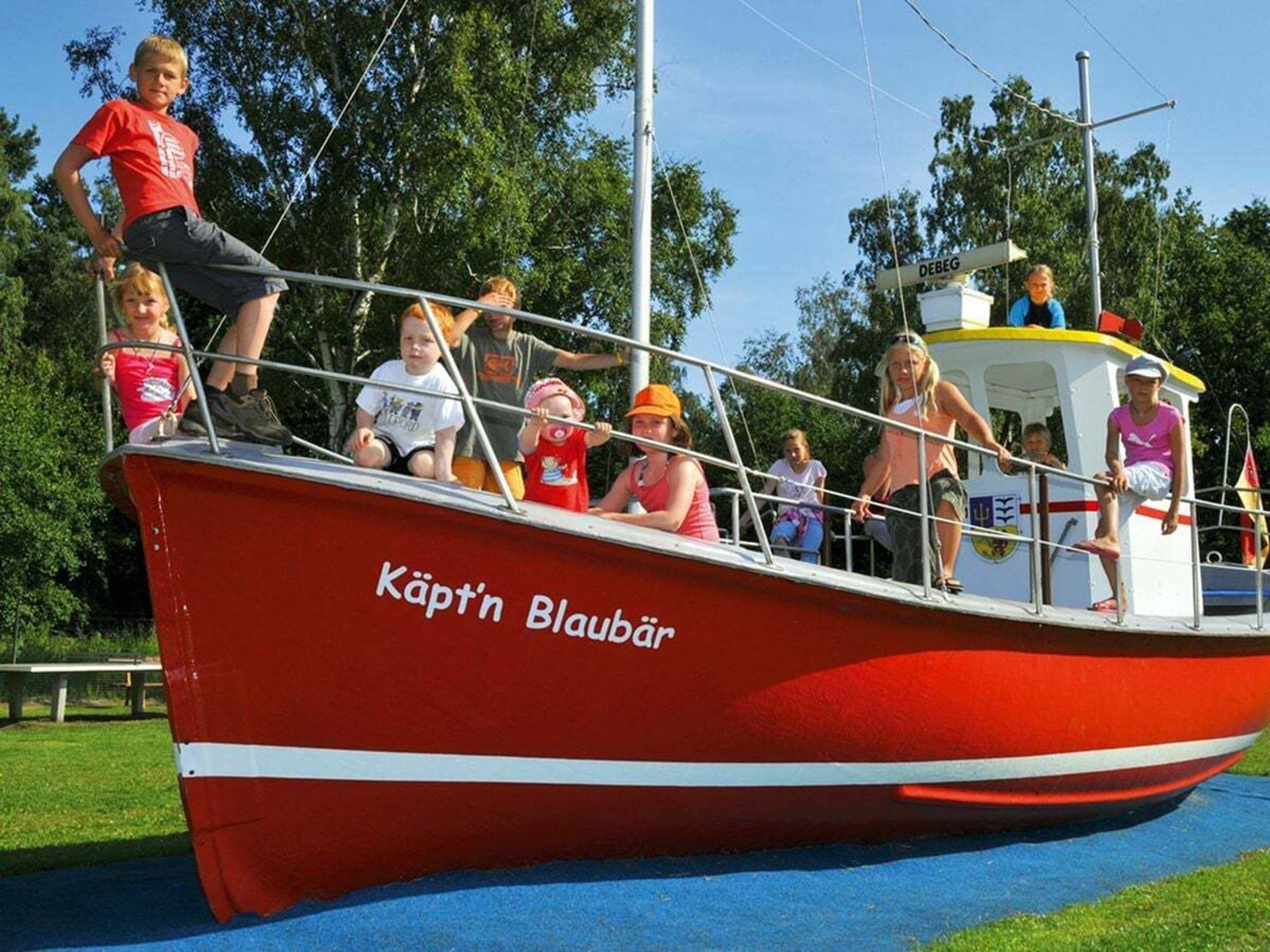A red boat with the name 'Käpt'n Blaubär' on its side, docked at a pier with people on board.
