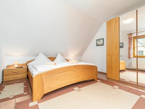 A bedroom with a wooden bed, a nightstand, a bedside table, a mirror, and a window with curtains. - 3.4/t3 Holiday Home Park \"freesenbruch\" (Zingst)